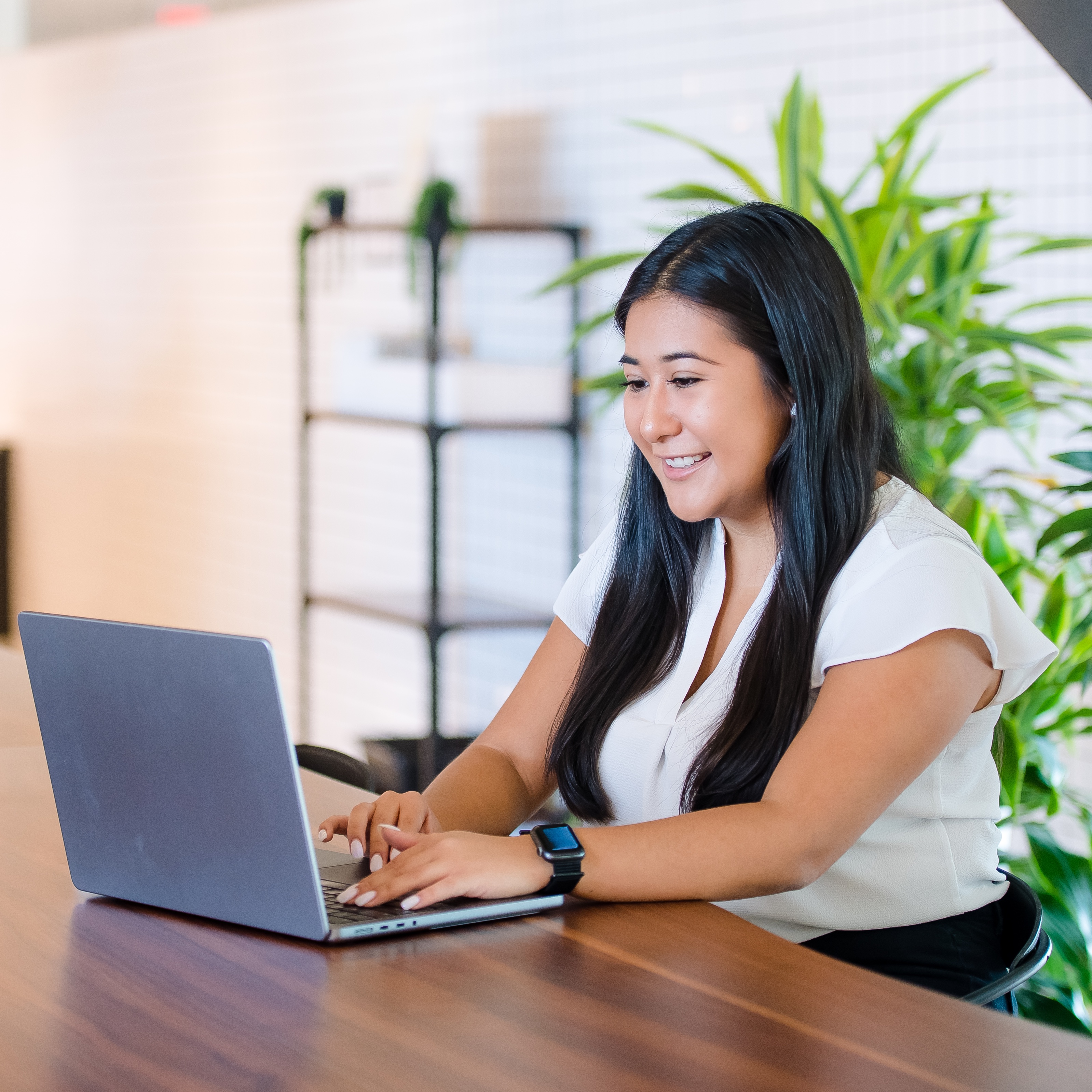 A Capital One associate sits at a table smiling and works on her laptop