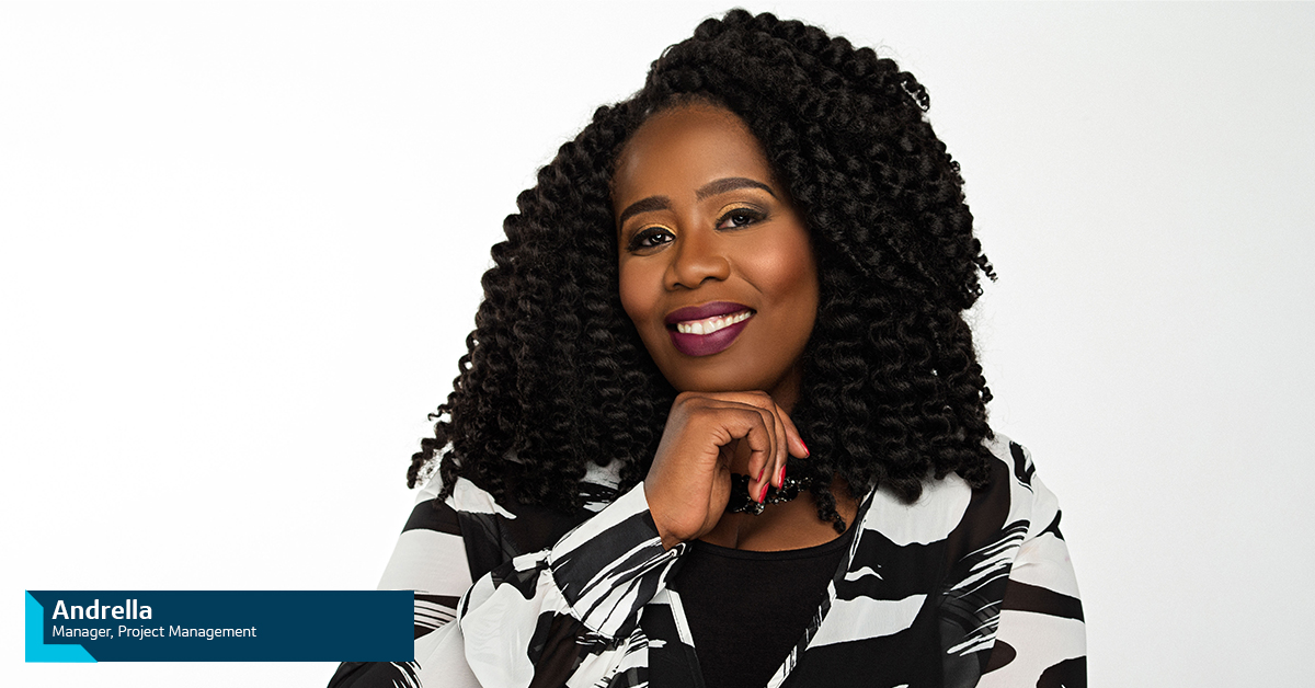 Andrella, Capital One Project Management Manager, smiling in front of a white wall with her hand under her chin