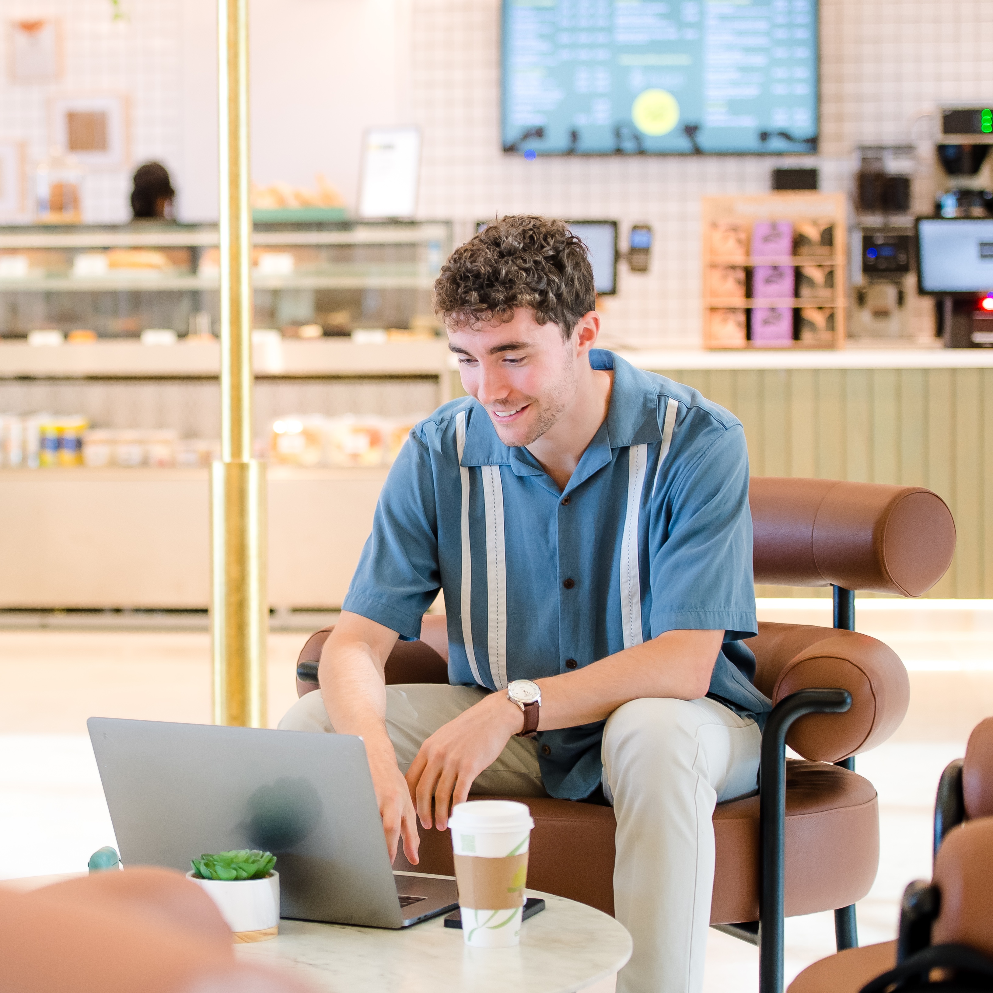 A Capital One MRP associate sits at a coffee table working on his laptop at a coffee shop
