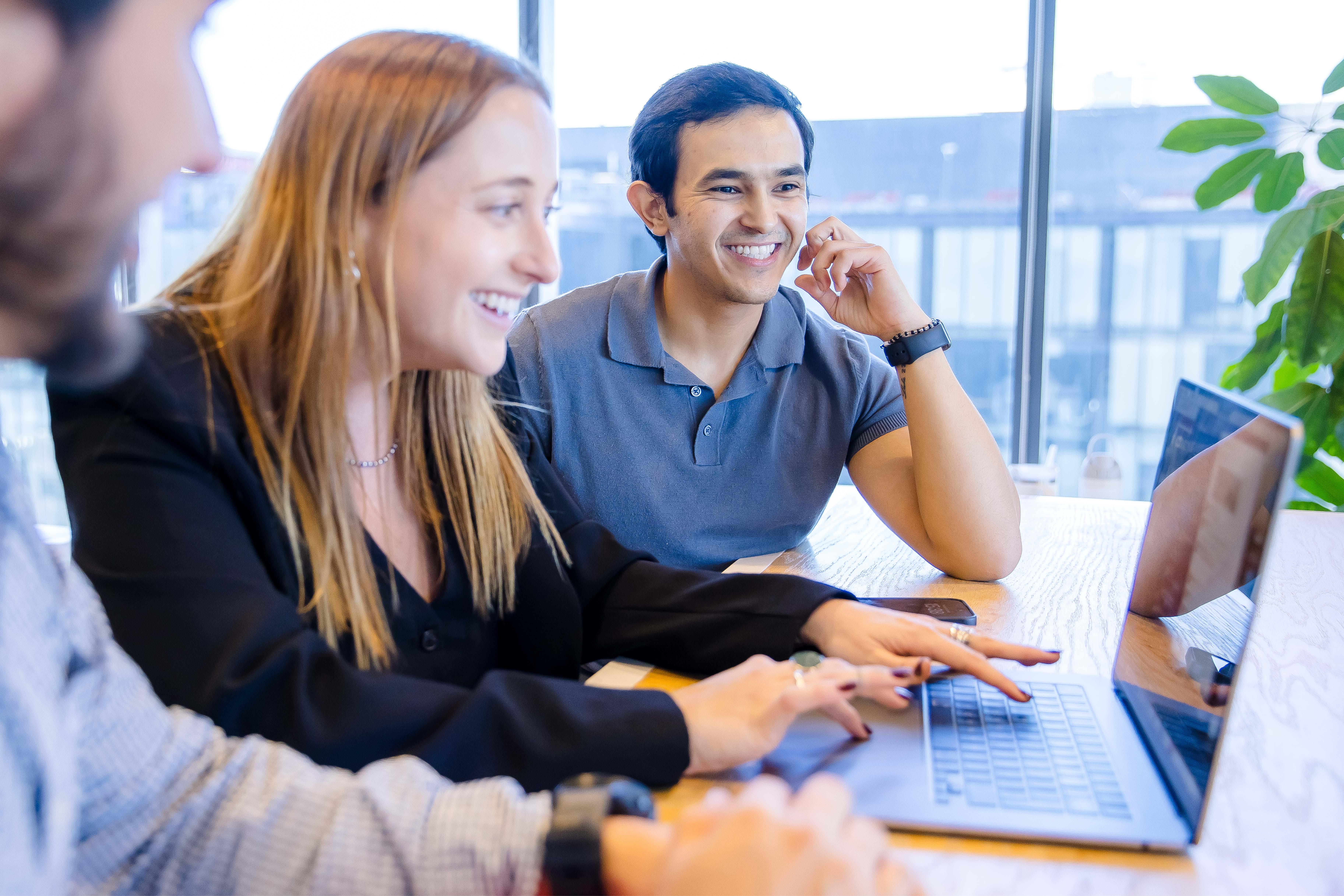 Three Capital One Mexico City associates sit at a table and look at a laptop together