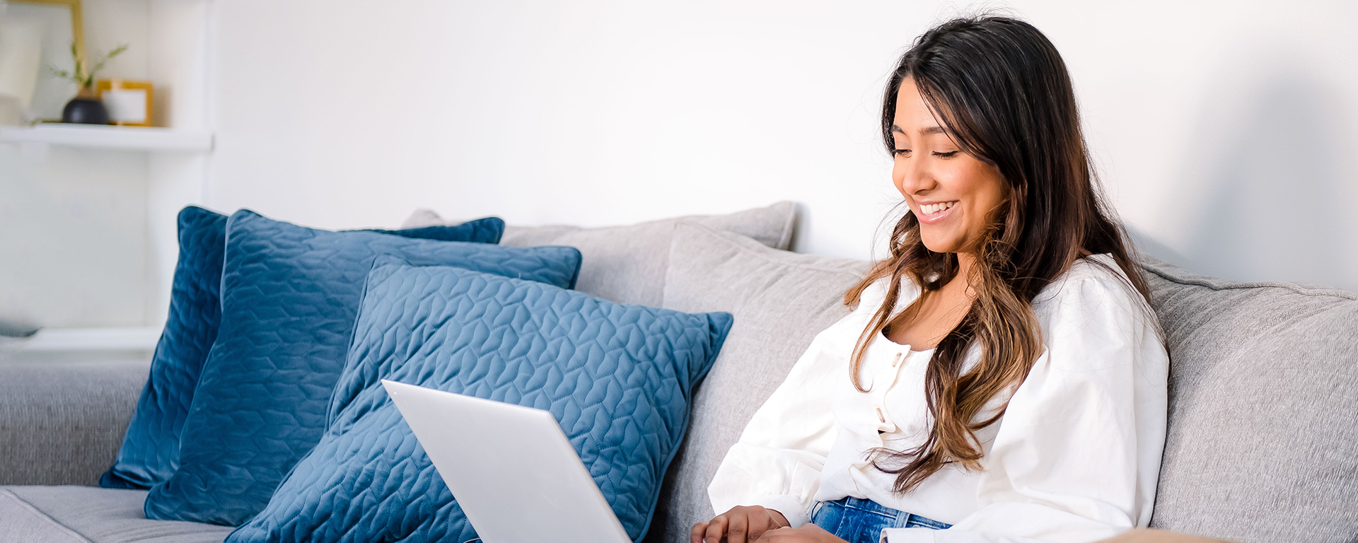 Capital One associate sits on a couch cross legged working on her laptop