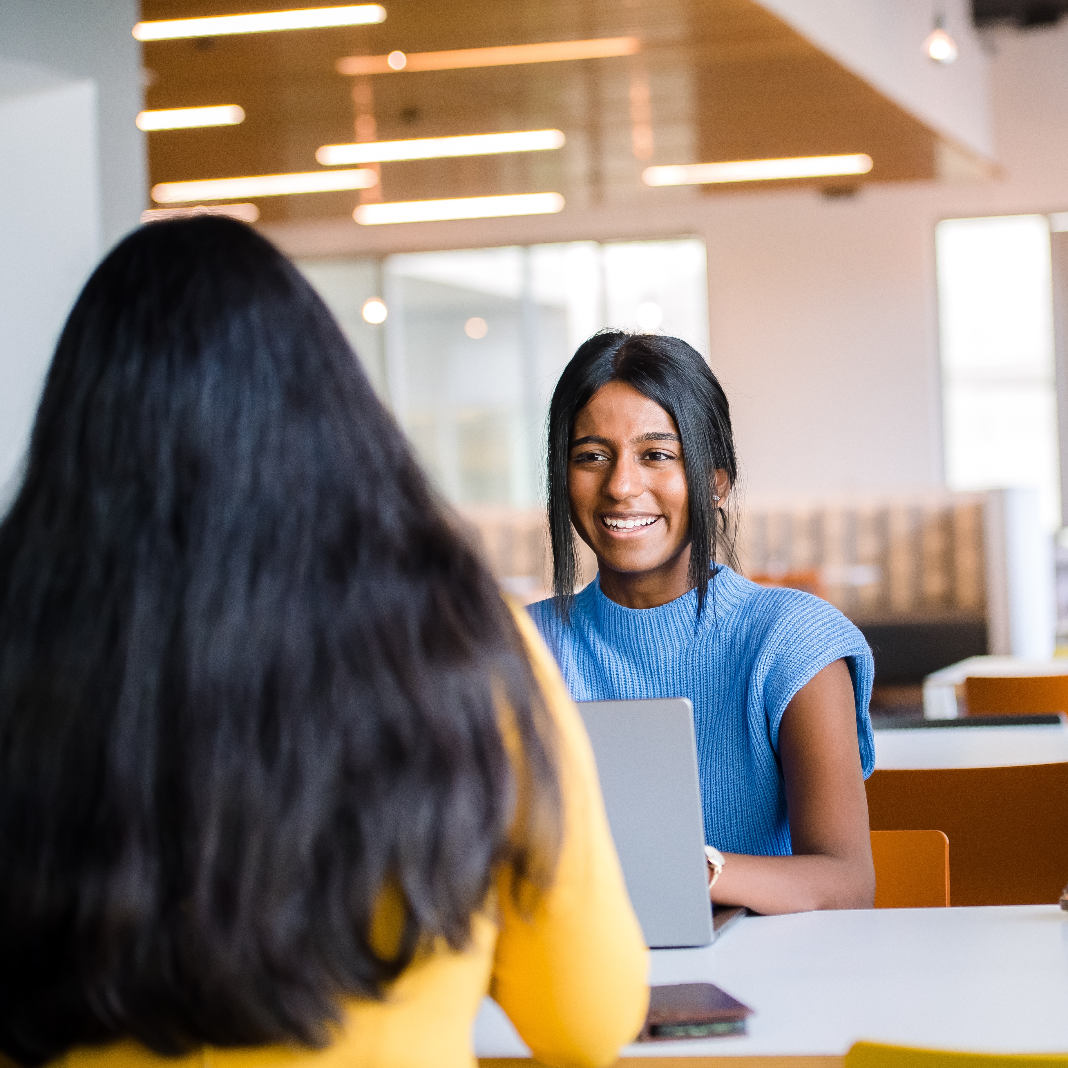 Two Capital One TDP associates sit at a table with their laptops and talk