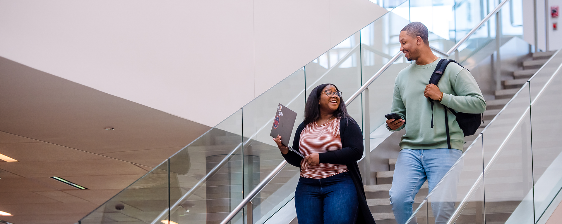 Two Capital One associats in casual clothes smile and talk as they walk down a set of stairs
