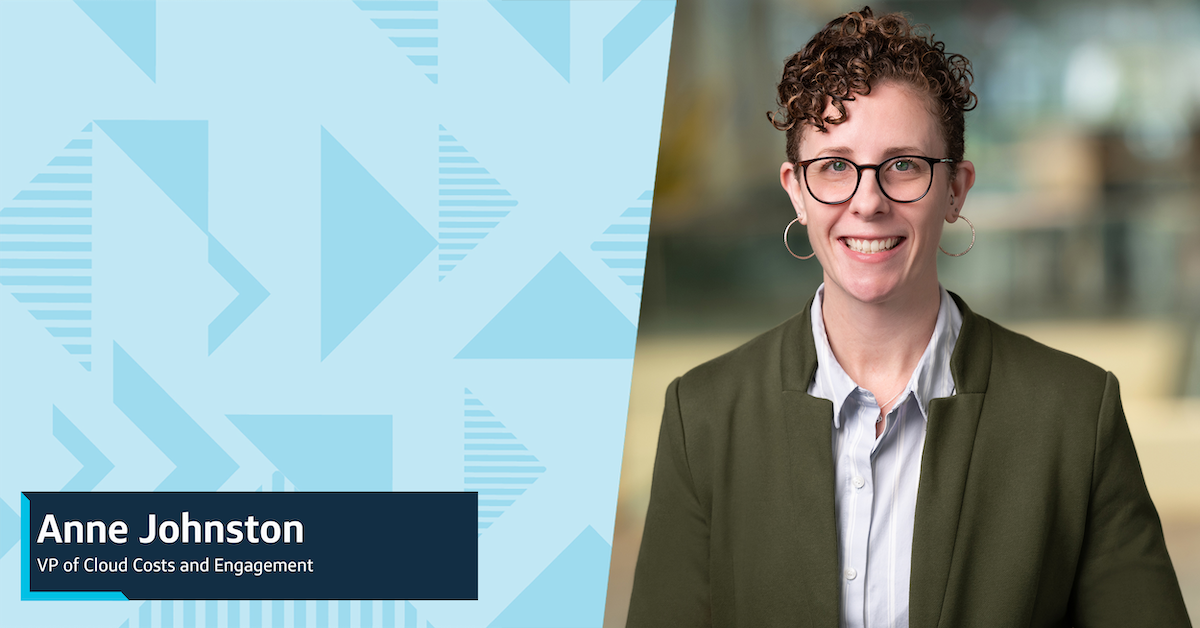 Capital One leader Anne smiles in front of a blurred background wearing a gray blazer and blue shirt
