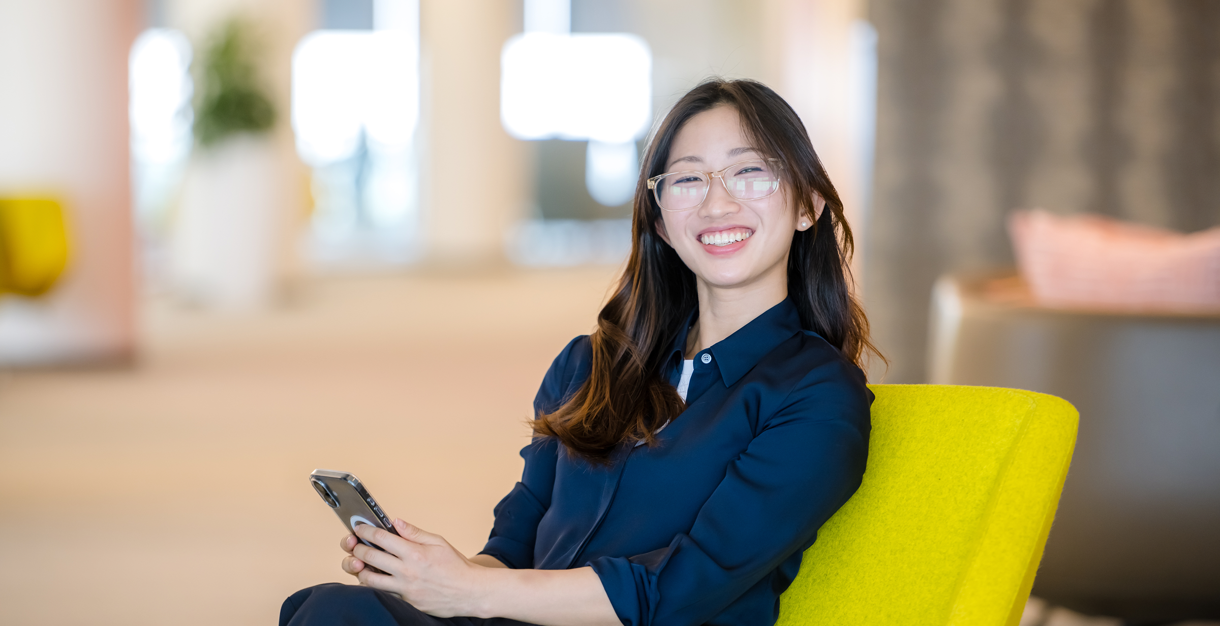 Capital One associate sits in a chair and smiles holding her phone 