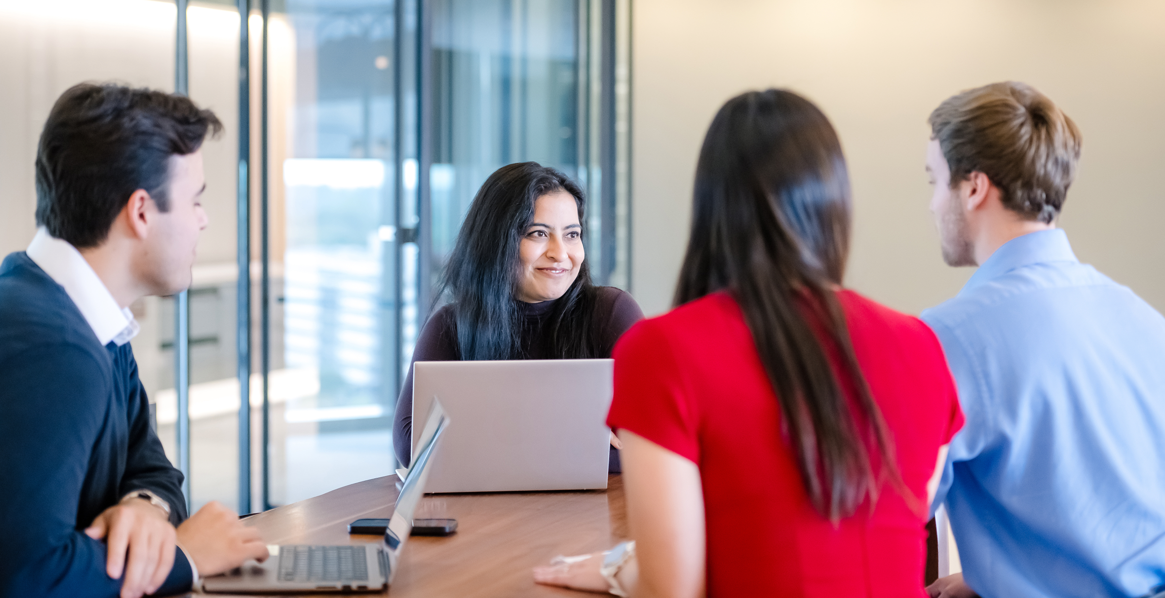 A group of Capital One associates work around a table together talking with their laptops