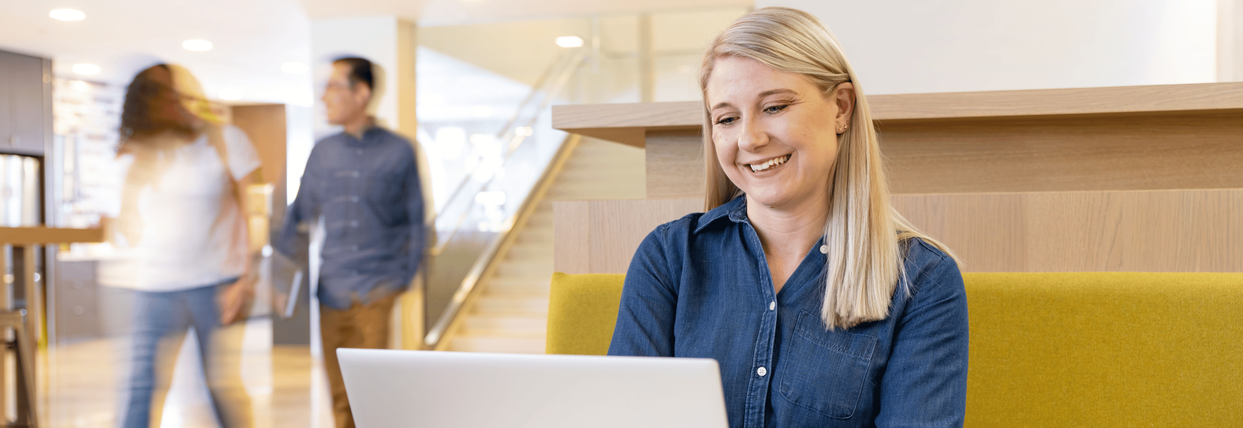 Capital One customer care associate sits and works on her laptop in a Capital One office as people walk by