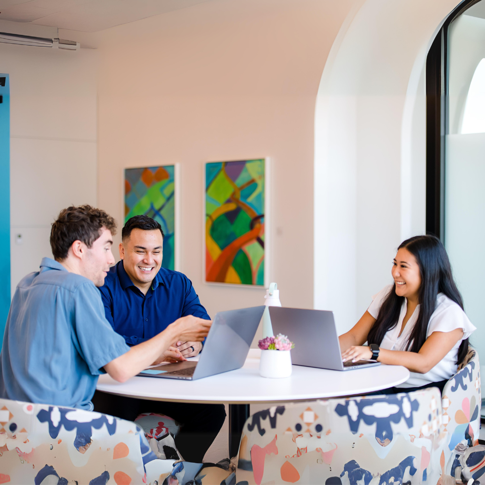 Three Capital One associates sit around a table and work together on their laptops