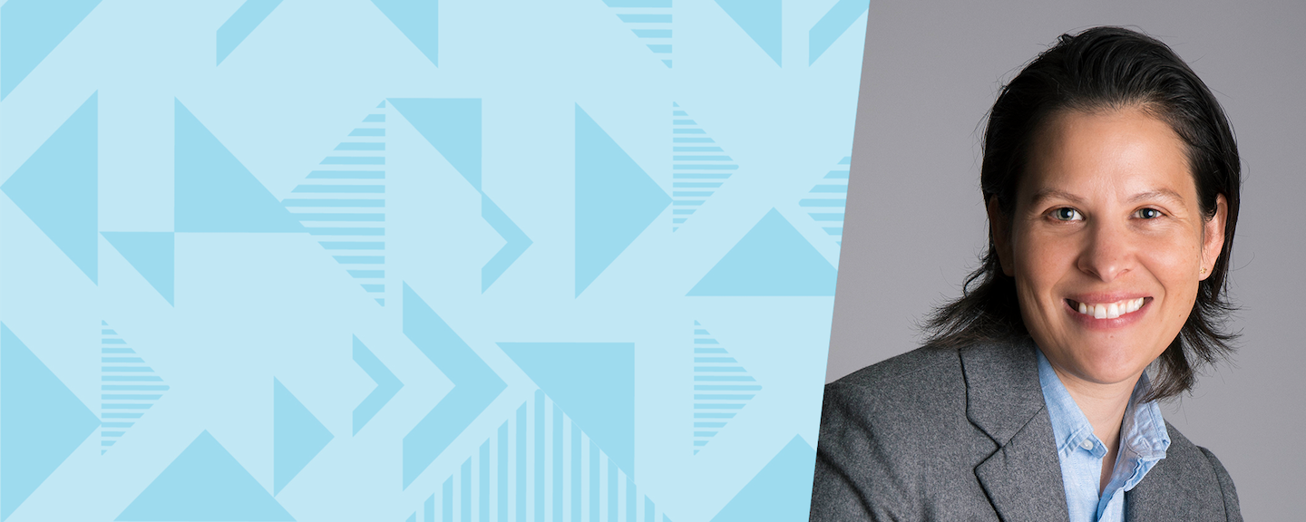 Capital One leader Joyce smiles in a gray blazer and blue shirt against a gray background