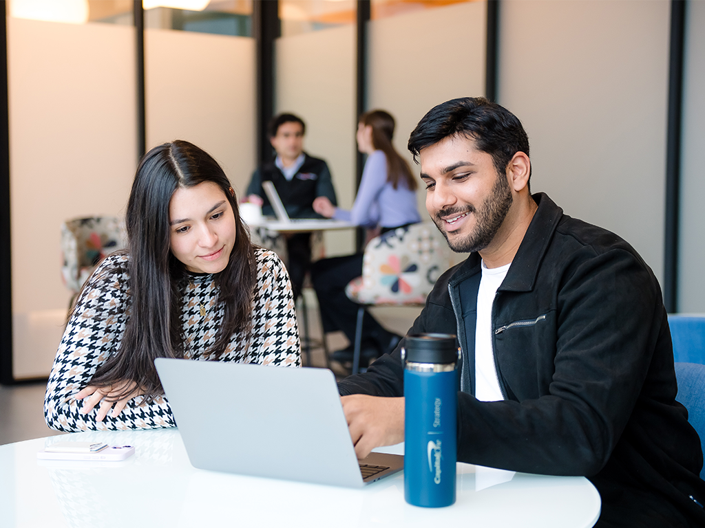 Two Capital One Strategy Consulting associates sit at a table and look at a laptop together