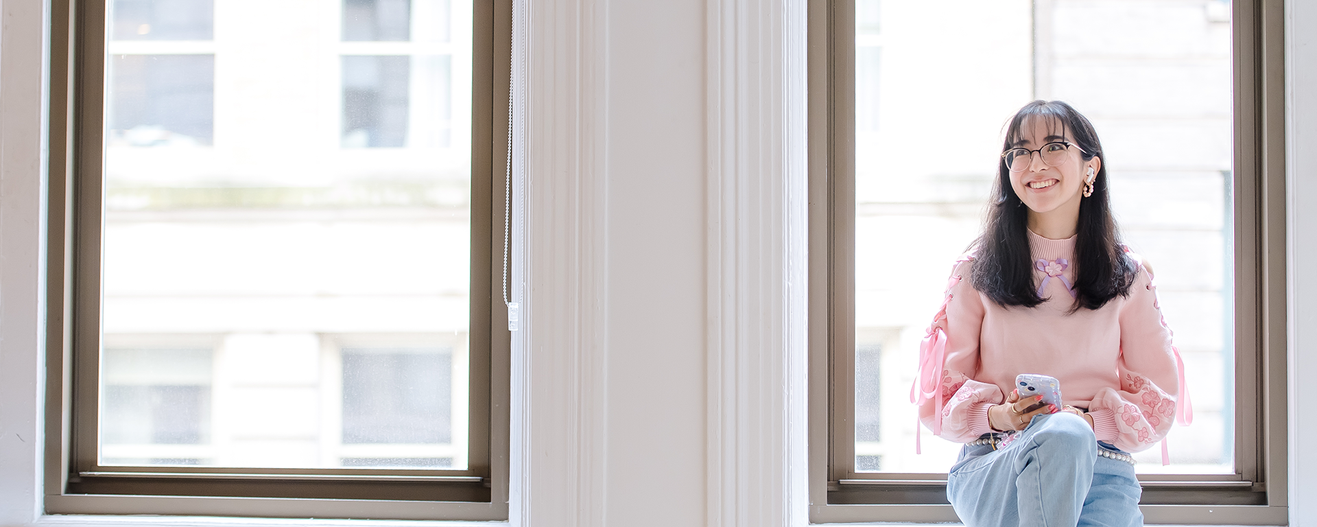 Capital One TDP Students & Grads associate sits in a window holding her phone wearing a pink sweater