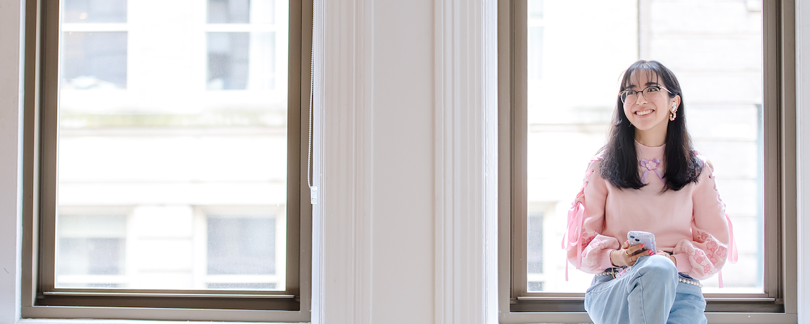 Capital One TDP Students & Grads associate sits in a window holding her phone wearing a pink sweater