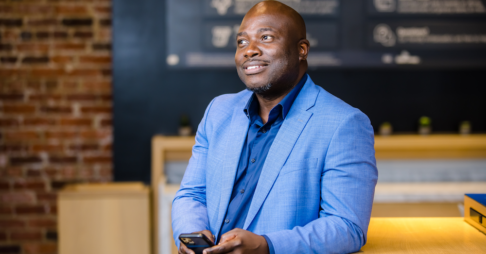 Capital One associate stands against a table and holds his phone